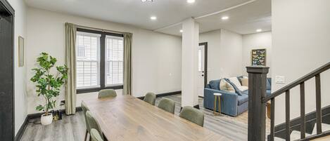 A spacious room with a wooden dining table, green upholstered chairs, a potted plant, and a staircase leading to another area.