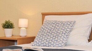 A neatly made bed with a patterned pillow, a bedside lamp, and a potted plant on a wooden nightstand.