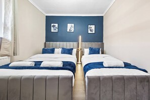 A hotel room with two beds, a grey headboard, and a blue accent wall. - Modern 2-Bed Apartment Sleeps 7 (London)