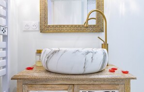 A bathroom with a marble sink, gold faucet, and a decorative mirror.