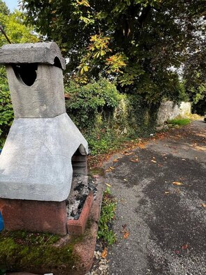 Uma estrutura de pedra com um buraco, base de tijolos e uma estrada pavimentada coberta de folhas caídas.