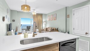 Una cocina moderna con una isla grande, encimeras blancas y lavavajillas integrado.
