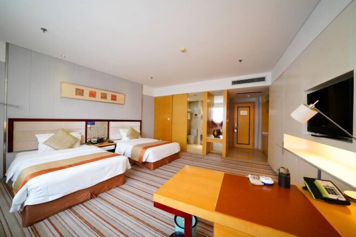 A hotel room with two beds, a desk, a TV, and a bathroom visible through an open door.
