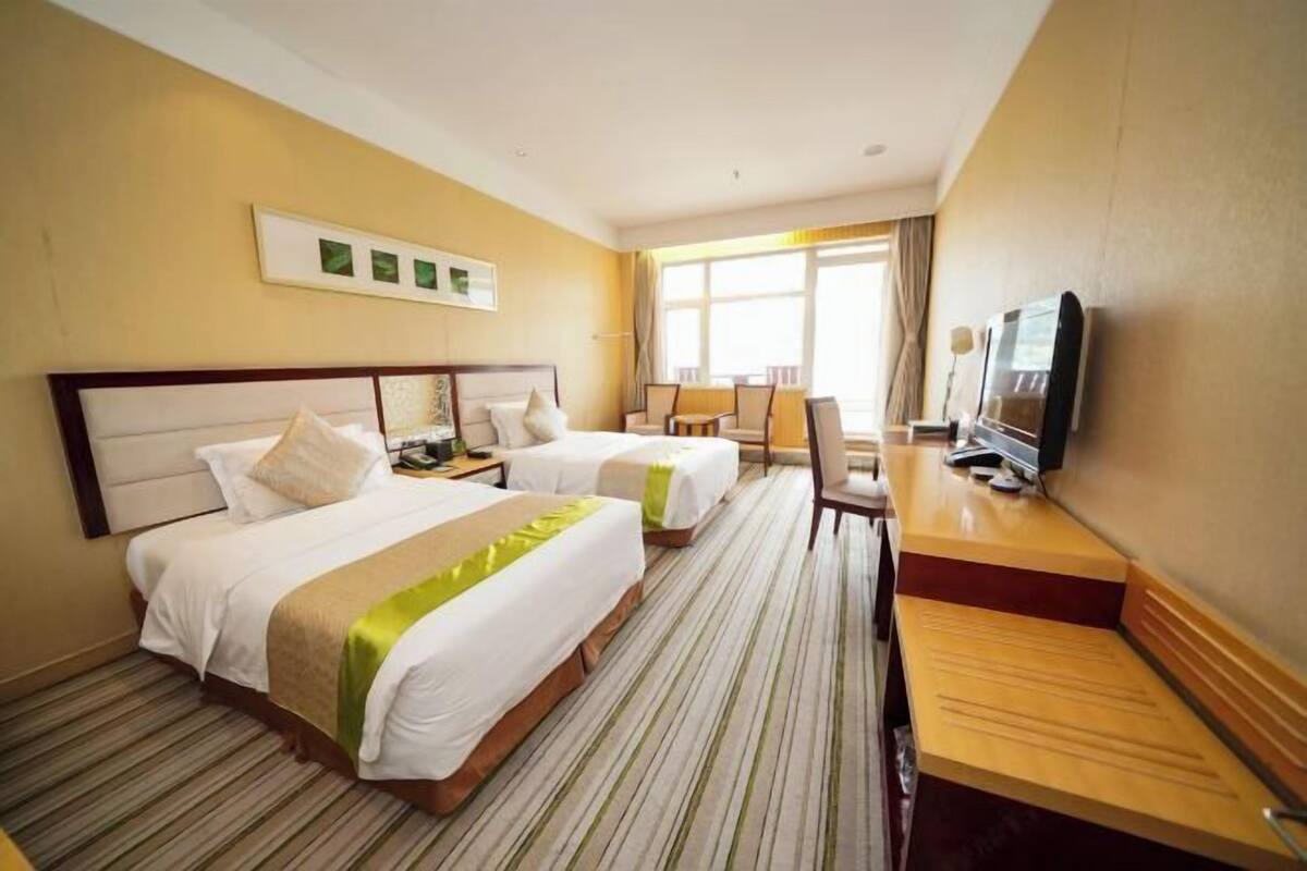 A hotel room with two beds, a desk, a television, and a window with curtains.