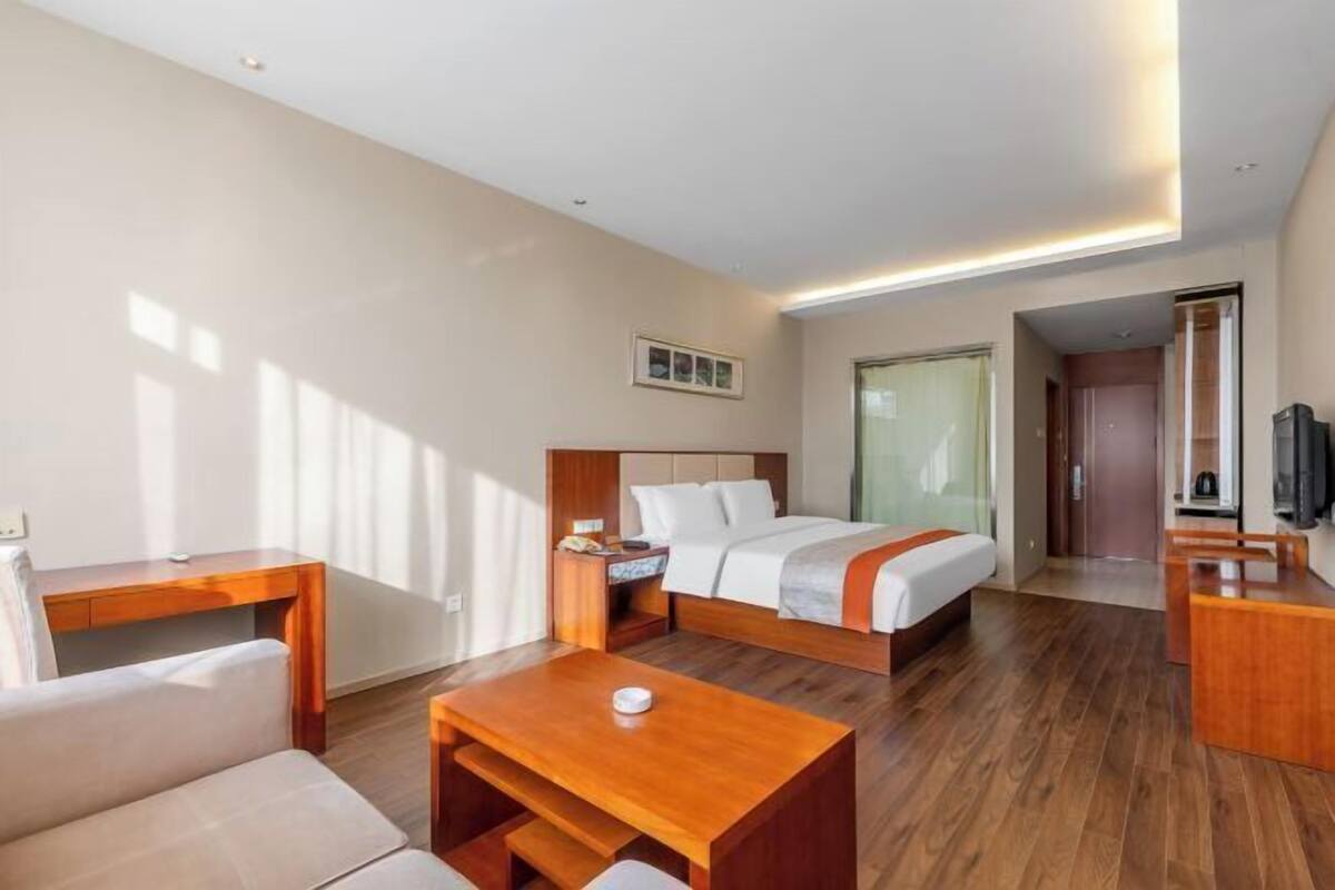 A modern hotel room with a bed, a desk, a chair, a small table, and a television.