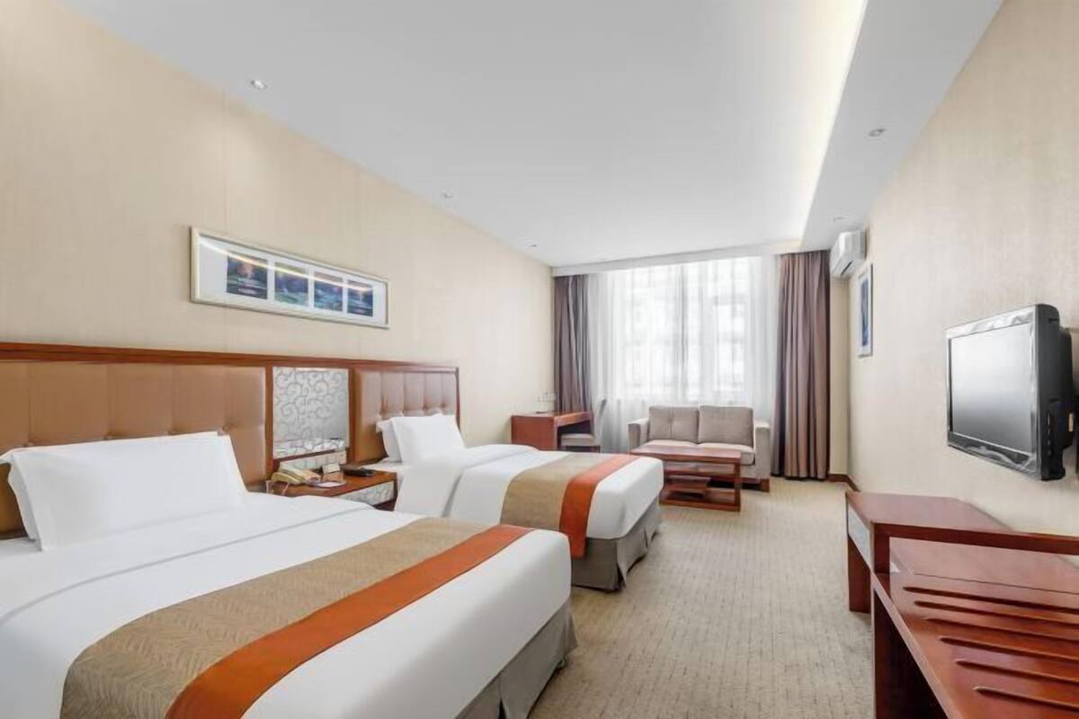 A hotel room with two beds, a sofa, a TV, and a desk.