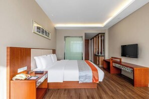 A hotel room with a large bed, a TV, a desk with a telephone, and a mirror.