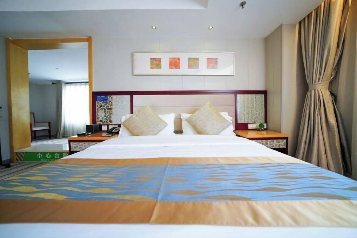 A hotel room with a large bed, a desk, a chair, and a mirror.