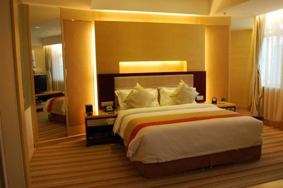A hotel room with a large bed, a bedside table with a lamp, and a mirror reflecting the room.