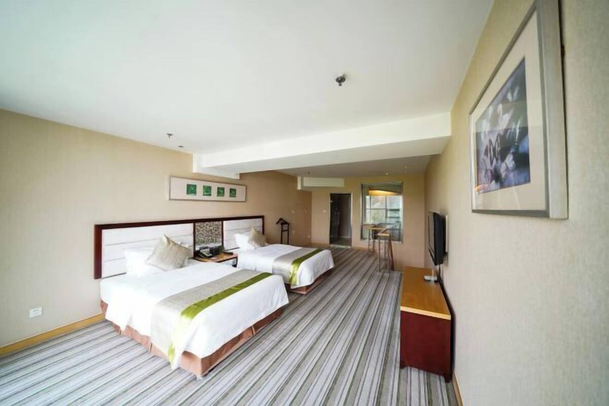 A hotel room with two beds, a desk, a chair, a TV, and a framed picture on the wall.