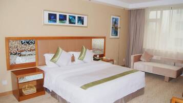 Quarto de hotel com uma cama grande, sofá, mesa de cabeceira e televisão fixada na parede.