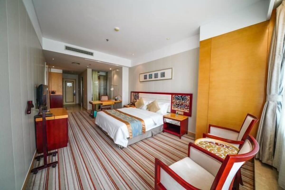 A hotel room with a bed, a desk, a chair, a nightstand, and a television.