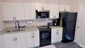 A compact kitchen with white cabinets, a black stove, a black refrigerator, and a microwave.
