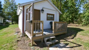 A small, single-story wooden cabin with a porch and a small deck.