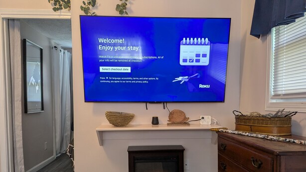 A living room with a flat-screen TV displaying a welcome message, a fireplace, and a wooden dresser.