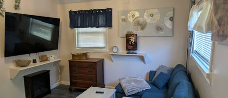 Una sala de estar con televisión de pantalla plana, chimenea, sofá, mesa de centro y elementos decorativos en las paredes.