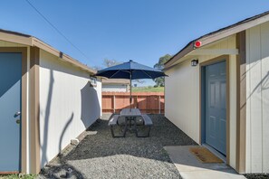 A compact outdoor area with a picnic table and umbrella, surrounded by a wooden fence and a single-story building with a blue door. - Studio 2 Mi to Feather River: Bring Your Pet! (Oroville)