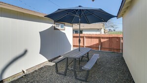 Een terras met een tafel en bankje onder een grote parasol, omringd door een witte schutting en een houten schutting op de achtergrond.