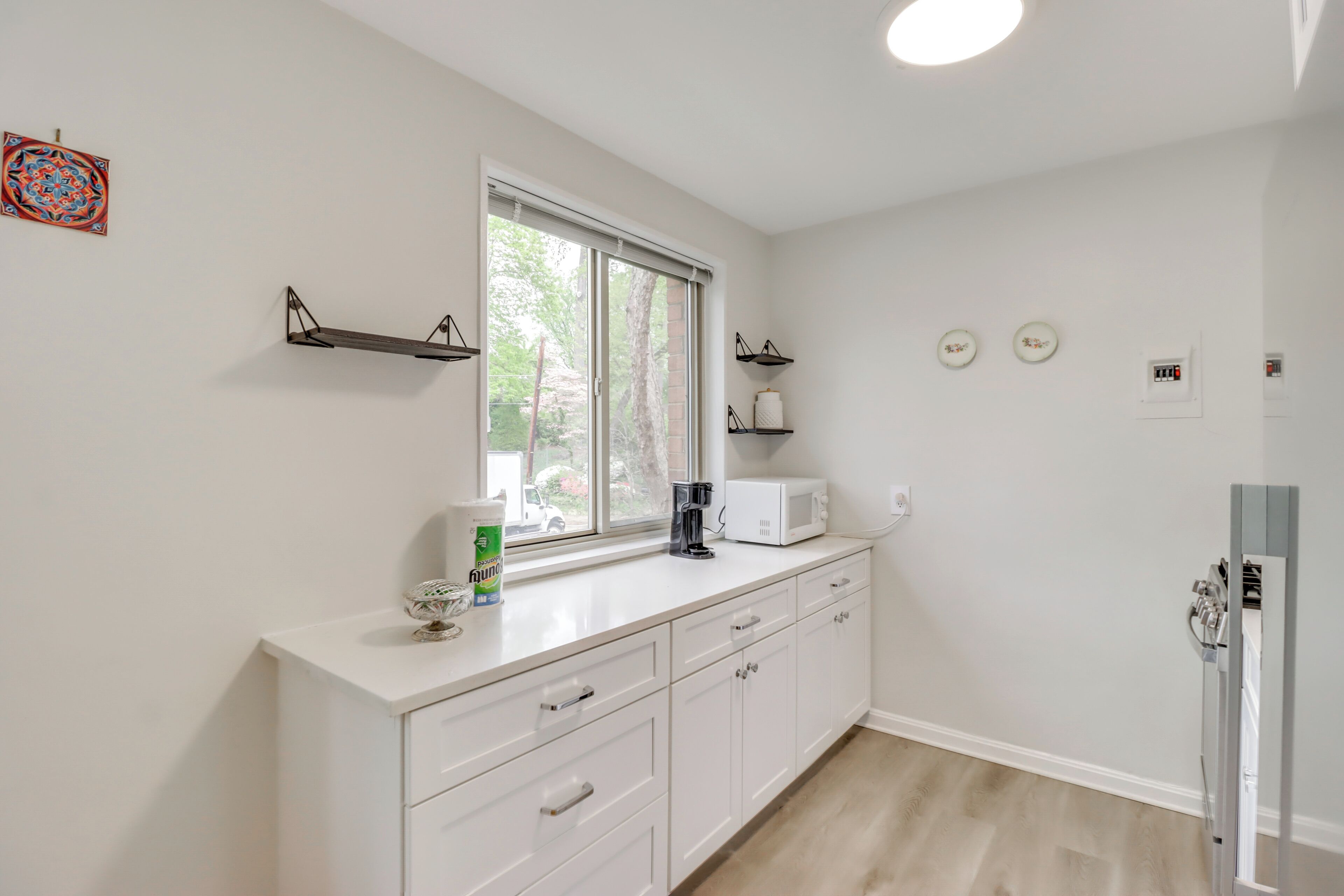 A modern kitchen with white cabinetry, a window with blinds, a microwave, and a coffee maker on the counter.