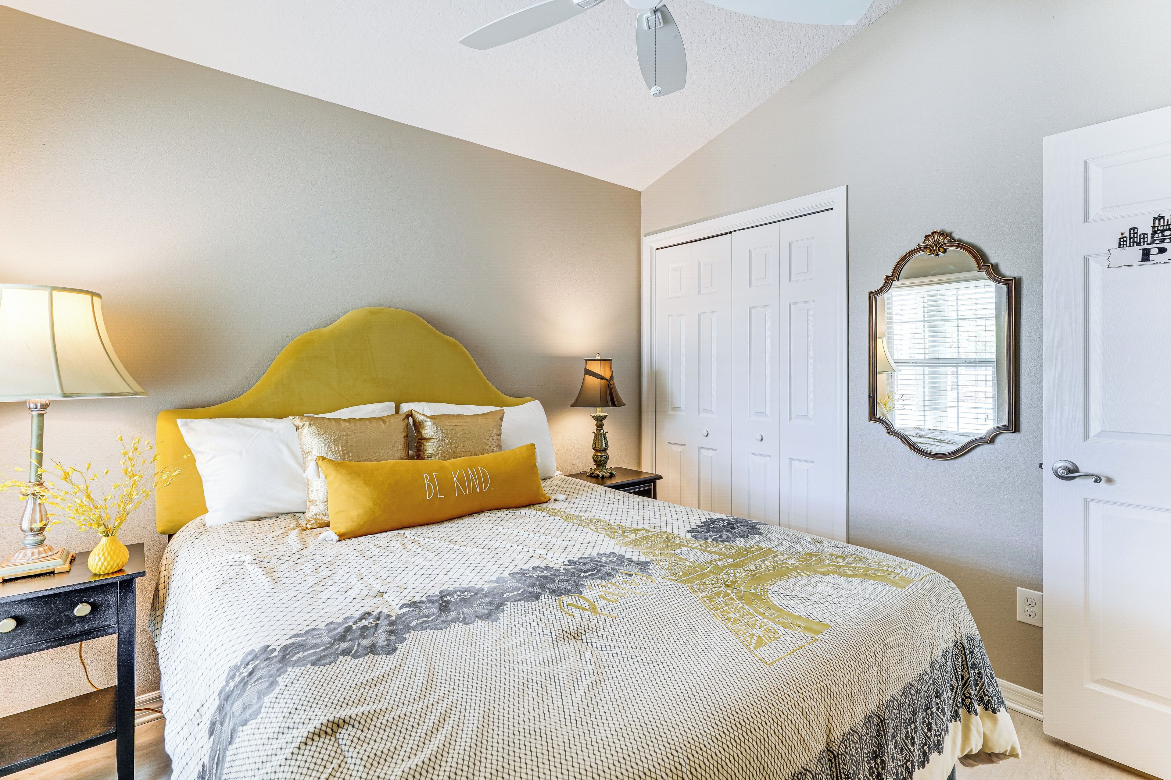 A bedroom with a bed, bedside tables, a ceiling fan, a door, and a mirror.