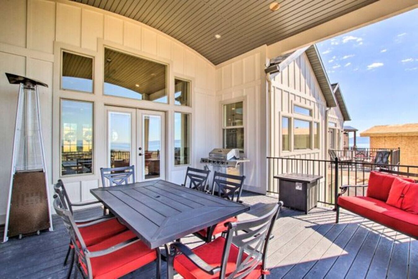 A covered outdoor area with a table and chairs, a grill, and a red sofa.