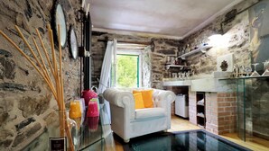 A room with a stone wall, a white sofa with yellow cushions, a glass table, and a glass railing overlooking a pool.