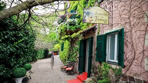 A narrow cobblestone alley with a building covered in ivy and a sign reading "Il Maestro di Tourlach 1583".