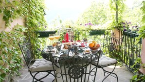A table set for breakfast on a patio with a view of greenery and a decorative stained glass window above.