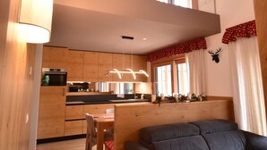 Eine moderne Küche mit Holzausstattung, ein Essbereich mit Tisch und Stühlen, ein graues Sofa und ein großes Fenster mit Vorhängen.