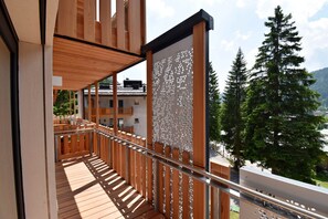 Ein Holzbalkon mit Metallgeländer, mit Blick auf eine gebirgige Landschaft mit Bäumen und Gebäuden.