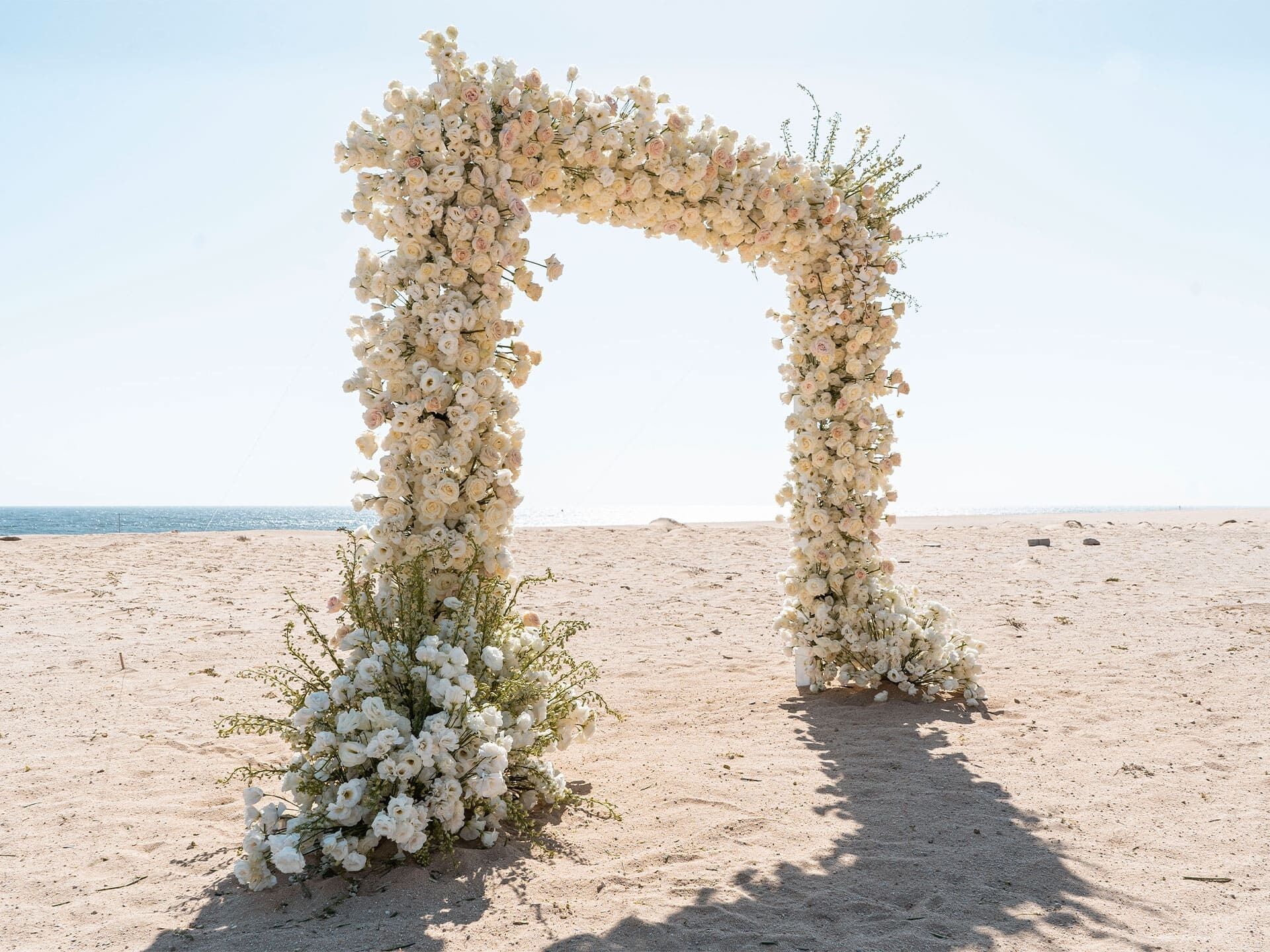 Ein blumengeschmückter Bogen an einem sandigen Strand.