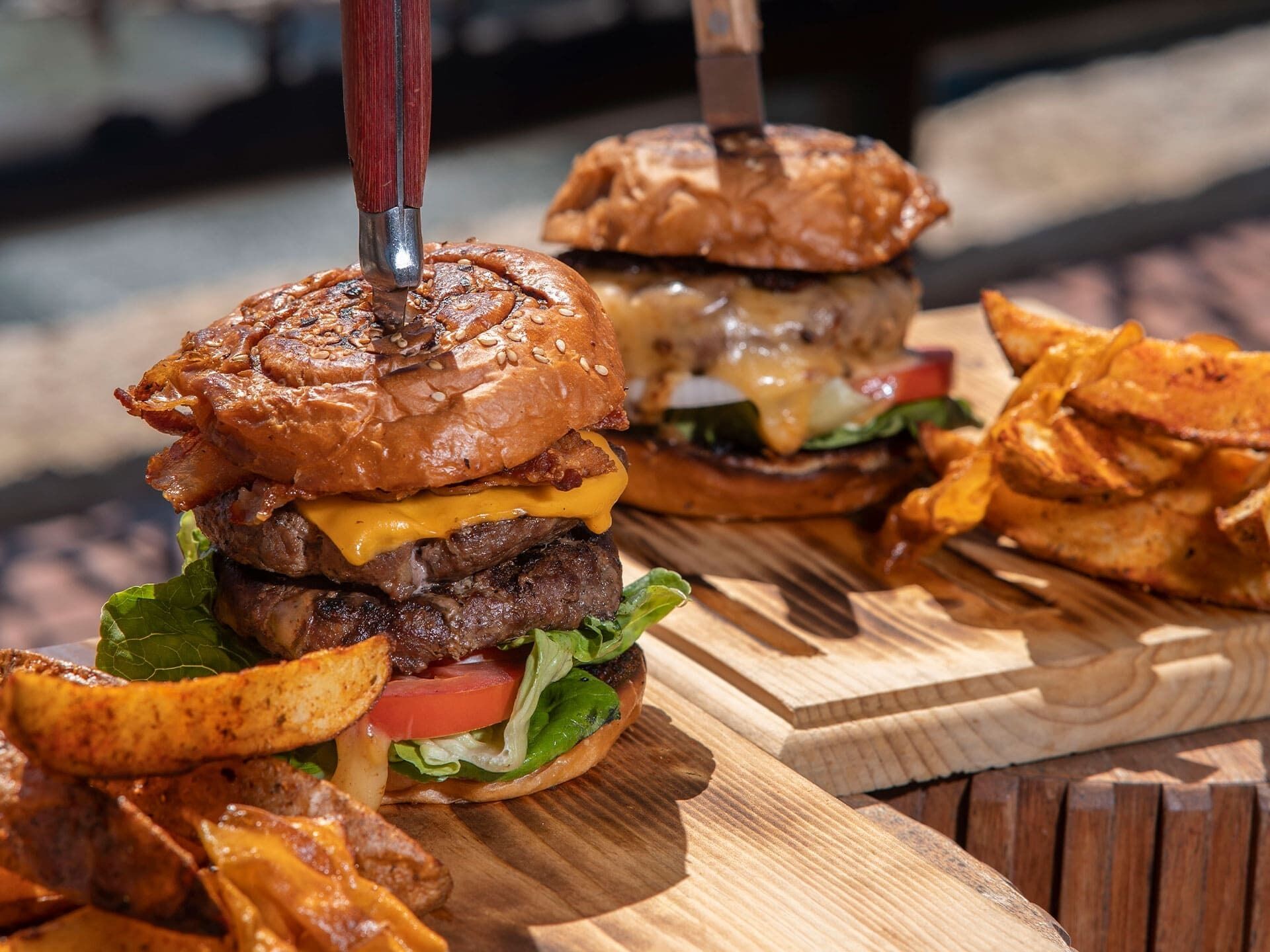 A burger with a knife inserted in the top bun, surrounded by fries and a wooden cutting board.