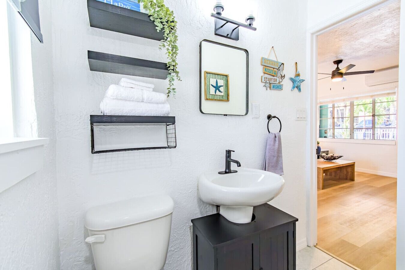 A bathroom with a white toilet, a black sink, and a mirror. There are shelves with towels and a starfish decoration.