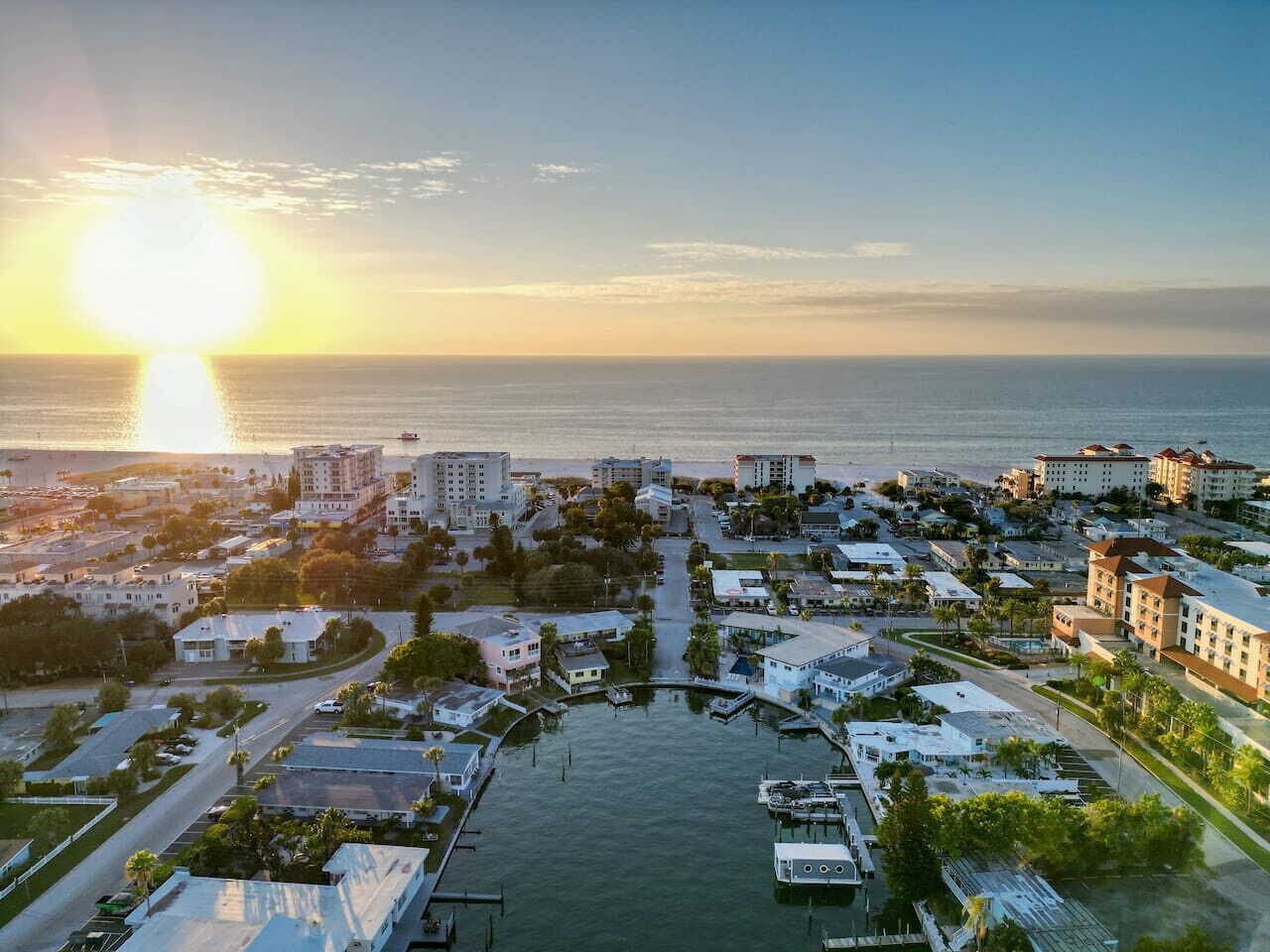 A coastal town with buildings, a marina, and a sunset over the ocean.
