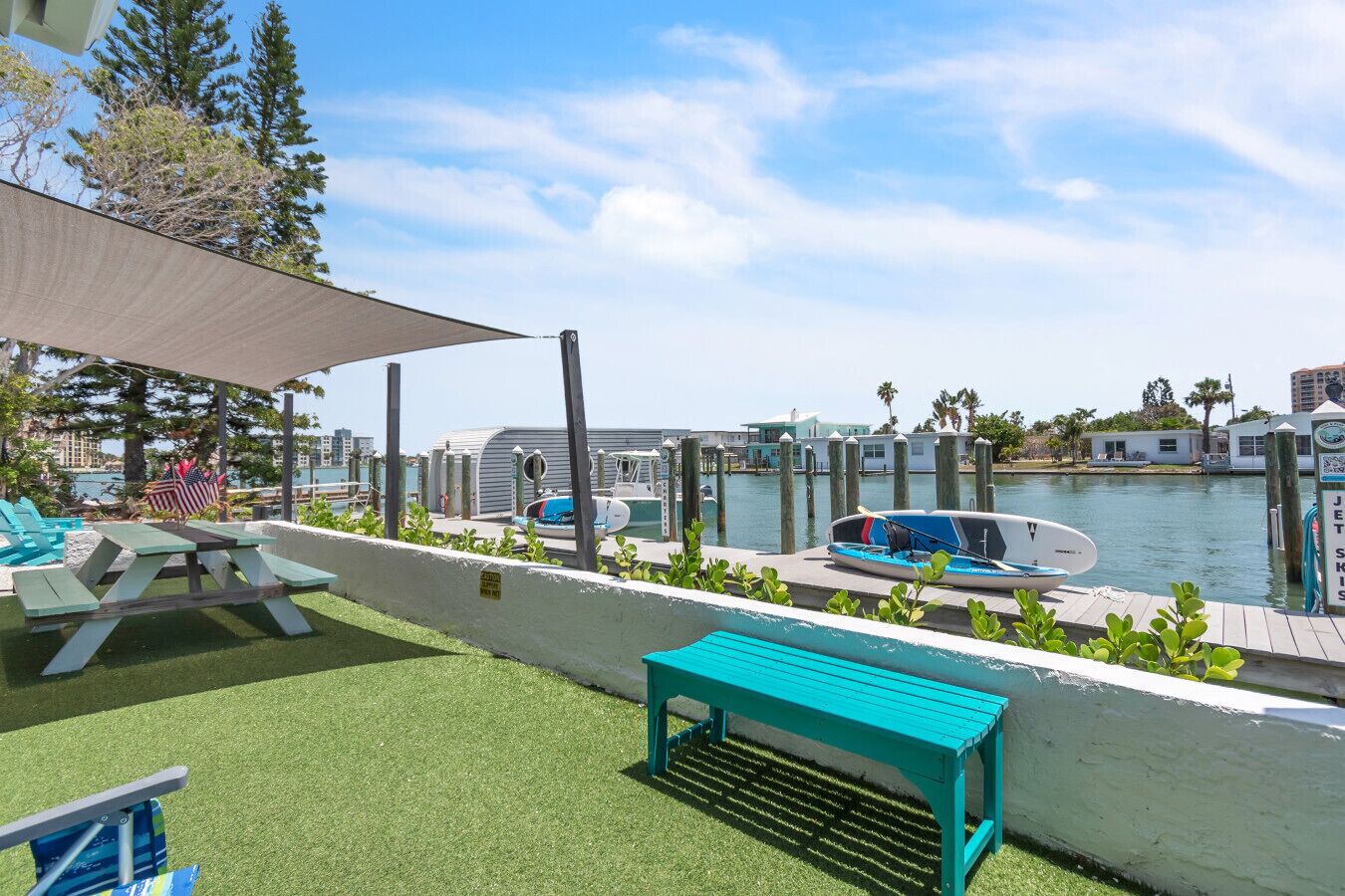 A waterfront patio with picnic tables, a boat, and a jet ski rental sign.