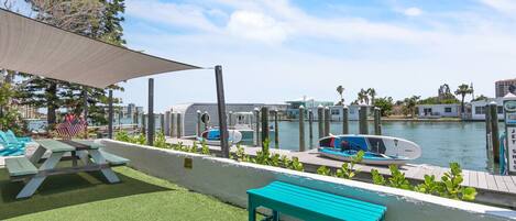A waterfront patio with picnic tables, a boat, and a jet ski rental sign.