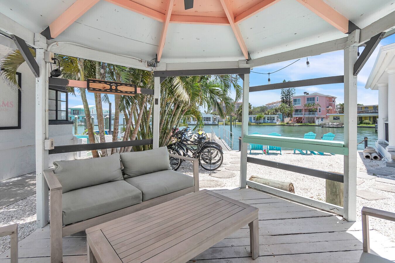 A covered outdoor seating area with a bench and a table, overlooking a body of water and a marina with boats.