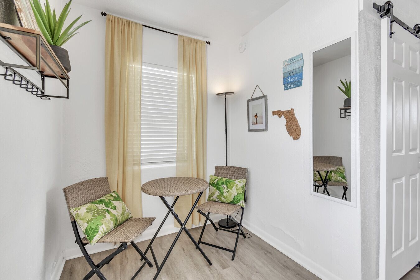 A compact living space with a window, two foldable chairs, a floor lamp, and a wall-mounted shelf with a plant.