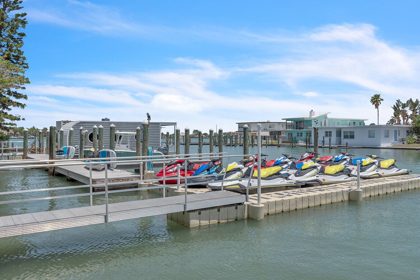 A marina with jet skis docked at wooden piers, a small dock with a boat, and buildings in the background.