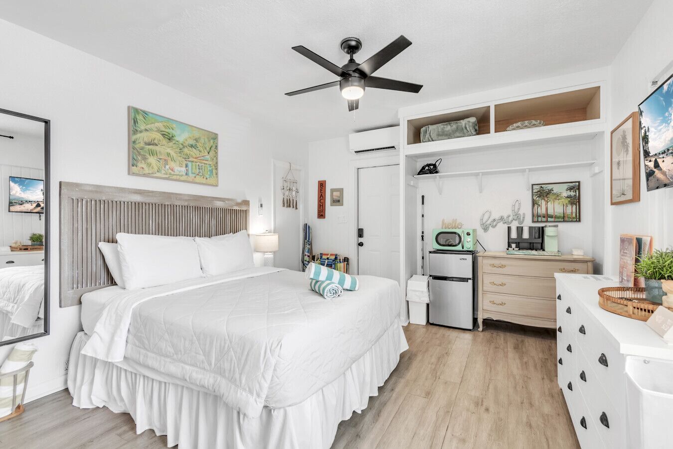 A bedroom with a bed, a ceiling fan, a dresser, a microwave, and a small refrigerator.