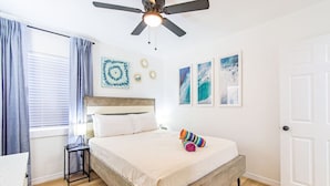 Ein Schlafzimmer mit einem Bett, einem Nachttisch, einem Deckenventilator und Kunstwerken an den Wänden.