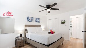 Ein Schlafzimmer mit einem Bett, einem Deckenventilator, einem Nachttisch, einem Spiegel und einer Tür zu einem Badezimmer.