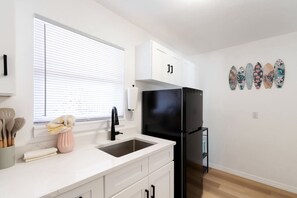Una cocina moderna con armarios blancos, un refrigerador negro, un lavamanos y una ventana con persianas.