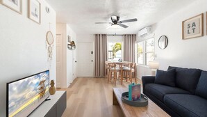 Ein modernes Wohnzimmer mit Fernseher, dunkelblauem Sofa, Couchtisch aus Holz und Deckenventilator.