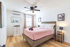 Une chambre d’hôtel comprenant un lit, des tables de chevet, un ventilateur de plafond, un appareil de climatisation, une armoire et une fenêtre avec des rideaux.