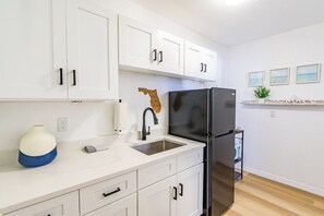 Une cuisine moderne avec des meubles blancs, un réfrigérateur noir et un évier.