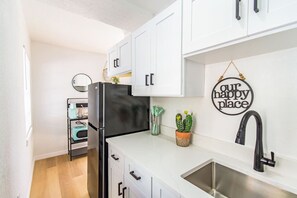 A modern kitchen with white cabinets, a black refrigerator, a sink, and a wall-mounted sign that reads "our happy place". - Waterfront Courtyard Condo 2 Blocks to Beach (Clearwater Beach)