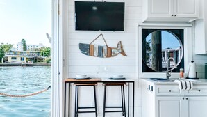 A compact kitchen with a TV, a dining table, and a view of the water outside.