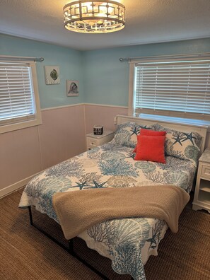 A bedroom with a bed, a nightstand, a lamp, and a window with blinds.