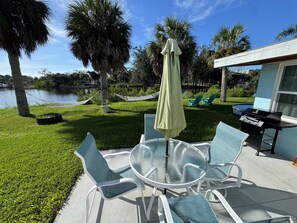 A patio with a round glass table and chairs, a grill, and a hammock. - Resting Place of Treasure Island NPR Waterfront Retreat w/ Kayaks & Sunroom (New Port Richey)